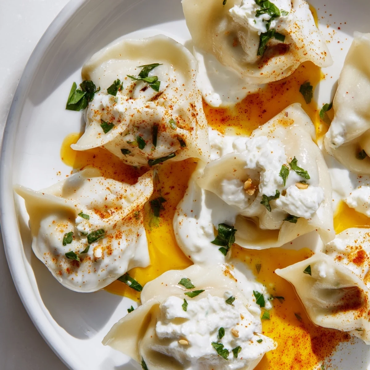 Golden-hued Turkish cheesy manti dumplings swimming in creamy yogurt and spiced butter, ready to eat.