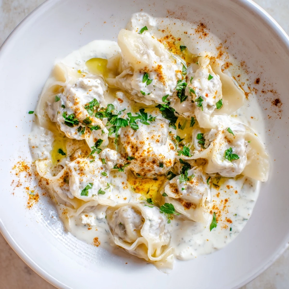 Close-up of freshly cooked Turkish cheesy manti dumplings, topped with vibrant paprika-infused butter and yogurt.