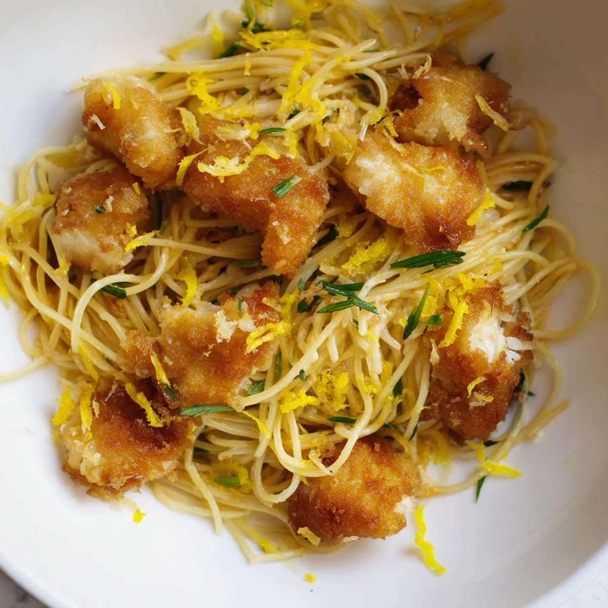 Crispy Fish Pasta featuring golden-brown fish flakes tossed with al dente spaghetti, fresh parsley, and bright lemon wedges on a rustic table.