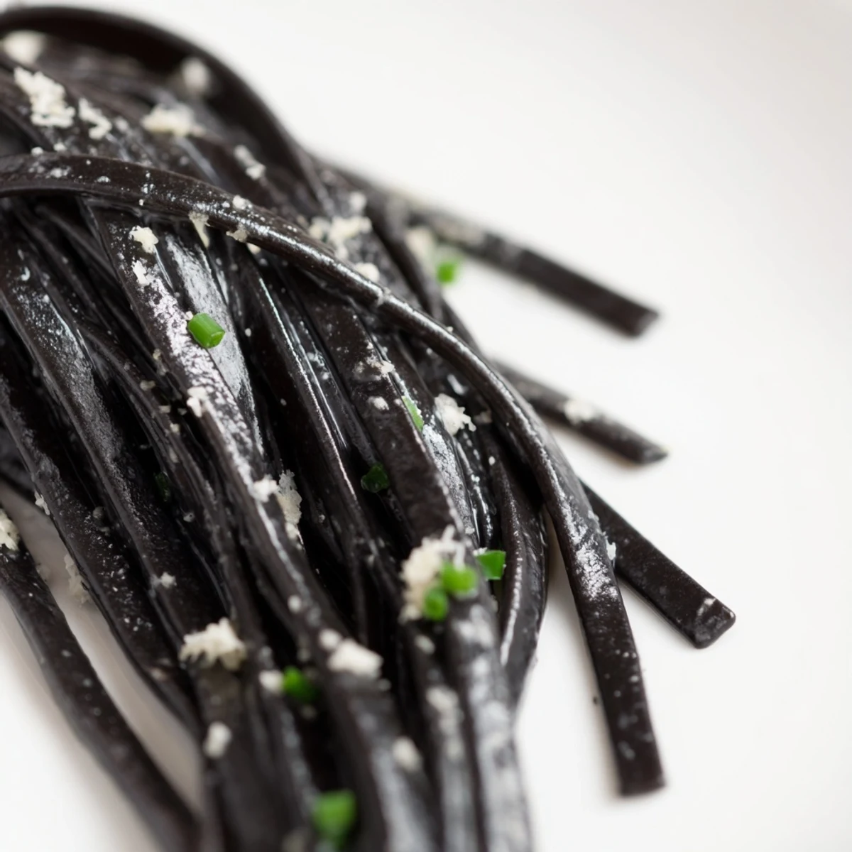 Squid ink pasta served on a white plate with lemon wedges and fresh chives, perfect for a luxurious dinner party.