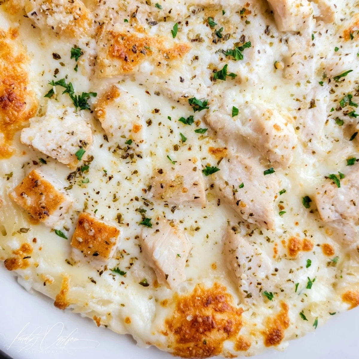 A slice of homemade Chicken Alfredo Pizza with golden, bubbly cheese and creamy sauce, topped with tender chicken on a rustic wooden board.
