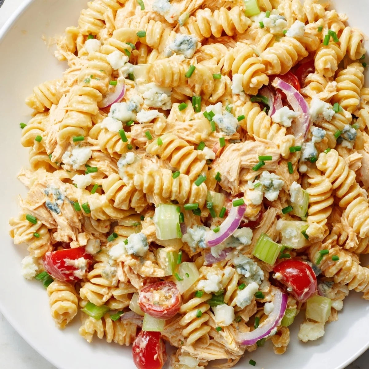 A close-up of creamy Buffalo Chicken Pasta Salad, featuring rotini pasta coated in tangy ranch dressing and vibrant chunks of chicken and red bell pepper.  