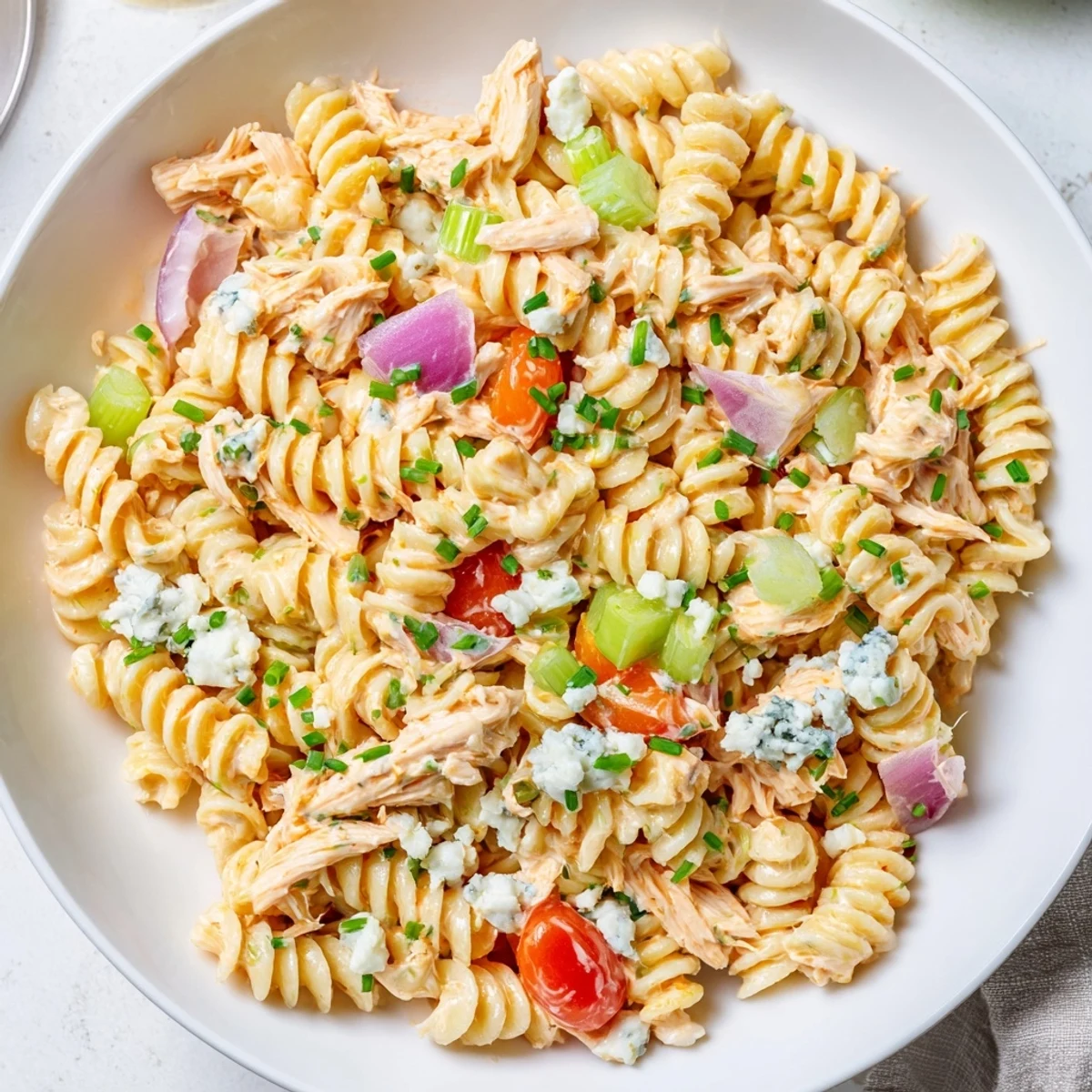 An overhead view of Buffalo Chicken Pasta Salad garnished with blue cheese crumbles and fresh chives, served in a clear bowl ready to enjoy.