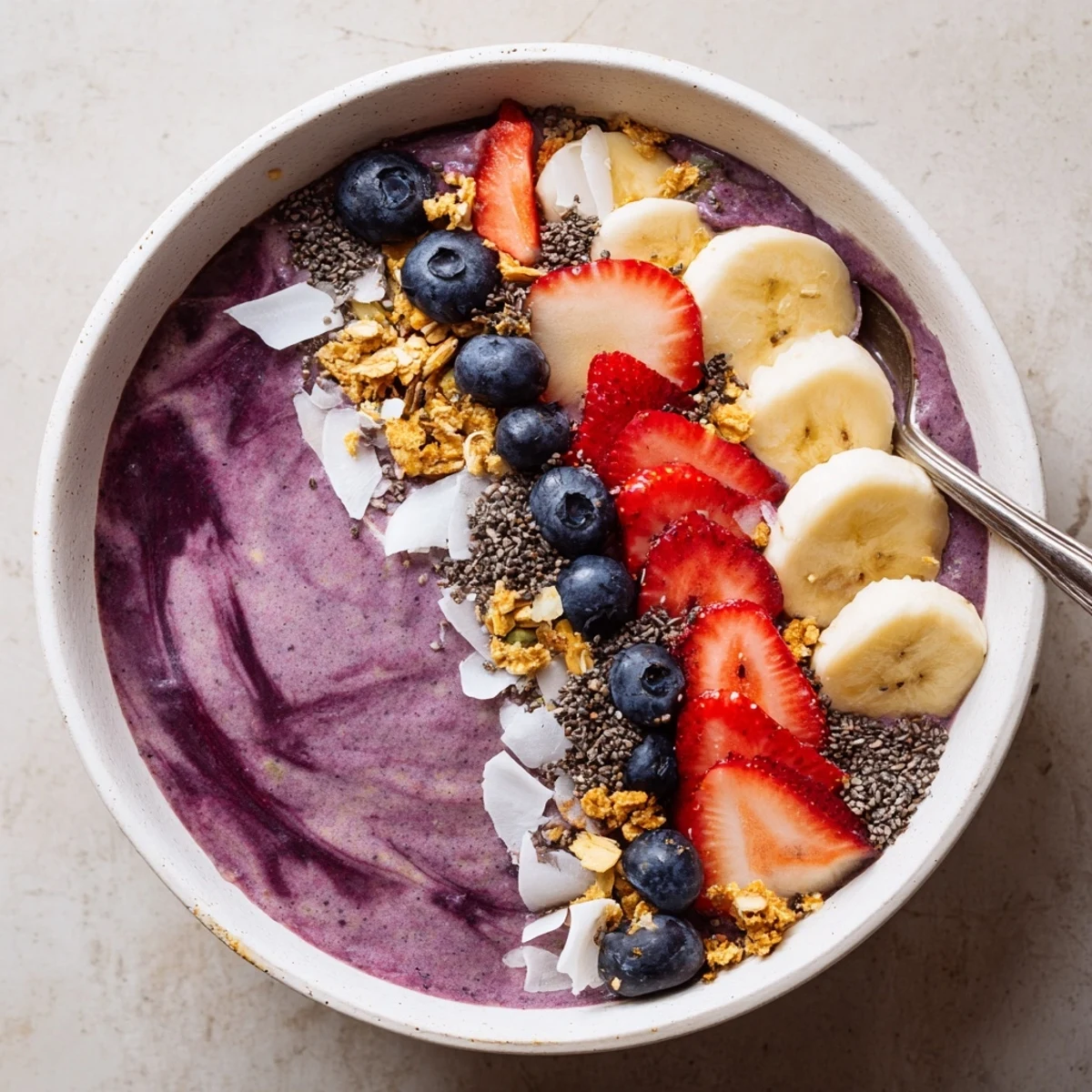 A thick, purple Acai Berry Smoothie Bowl with sliced bananas, fresh berries, and crunchy granola for a vibrant breakfast.  