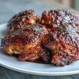Tender roasted chicken thighs with caramelized skin, glazed in homemade guava BBQ sauce on a baking sheet.