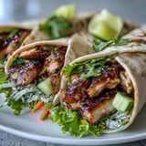 Two Sweet Chili Chicken Wraps are cut in half on a wooden board, paired with lime wedges and a crisp side salad.