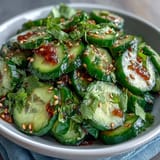 Crisp Asian cucumber salad with sesame and rice vinegar dressing, garnished with toasted sesame seeds and fresh cilantro. A refreshing, tangy side dish perfect for warm weather meals.