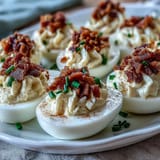 Savory deviled eggs topped with crumbled bacon and fresh chives, featuring a rich ranch-flavored yolk filling.