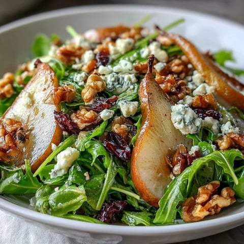 Fresh Arugula and Pear Bowl salad topped with creamy blue cheese and toasted walnuts on a white plate.