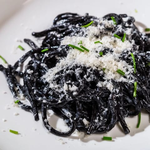 A fork twirls squid ink pasta in a rich, velvety cream sauce, highlighting its dramatic black strands and glossy finish.