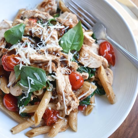 A close-up of Balsamic Glazed Chicken Pasta with cherry tomatoes, grated Parmesan, and fresh basil garnish.  