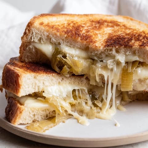 Buttery Havarti & Caramelized Leek Grilled Cheese slices, melty cheese oozing from crispy bread beside a fresh green salad.
