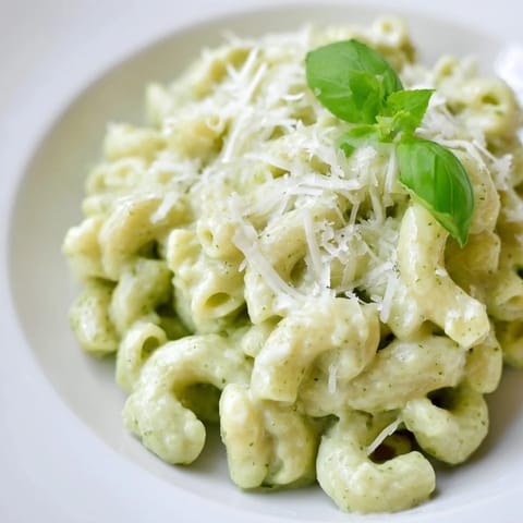 A vibrant bowl of creamy avocado pesto mac with tender pasta, bright green sauce, and a lemon wedge on the side.  