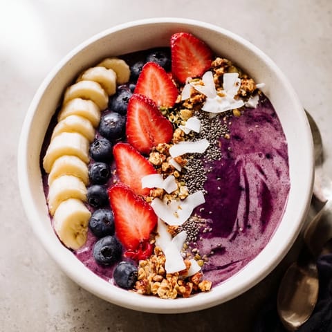 Vibrant Acai Berry Smoothie Bowl topped with strawberries, blueberries, and chia seeds, ready to enjoy with a spoon.  