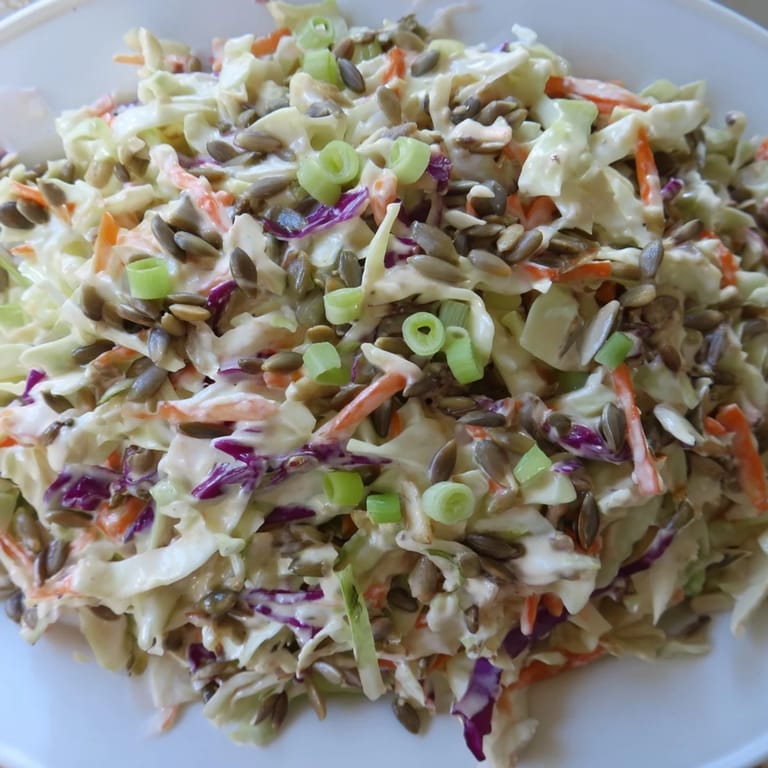 This vibrant bowl of crunchy coleslaw salad shows shredded cabbage and carrots topped with sunflower seeds.
