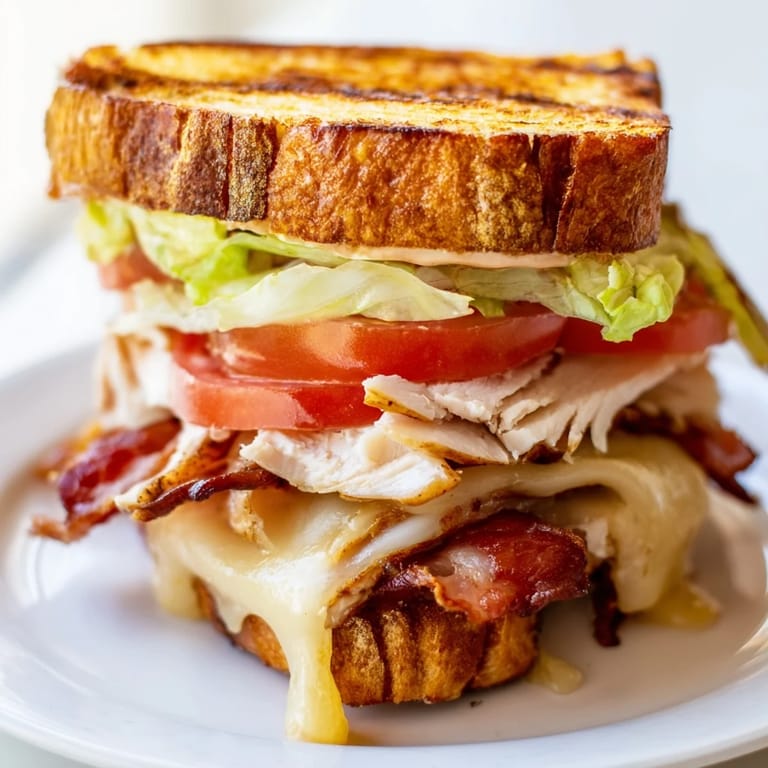 A close-up view of a toasted Turkey Club Grilled Cheese, stacked high with turkey, bacon, lettuce, and tomato.