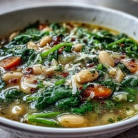 A steaming bowl of Tuscan white bean and spinach soup with vibrant greens and tender vegetables.